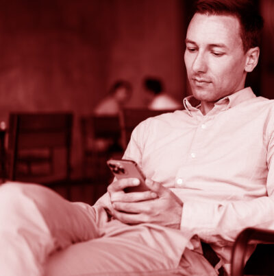 Man sitting in a chair looking at his phone, with a red overlay, inviting visitors to subscribe to our newsletter.