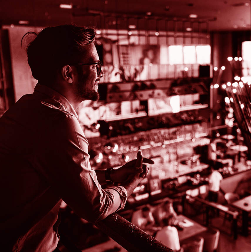 Restaurant owner smiling as he overlooks his establishment, with a red overlay.